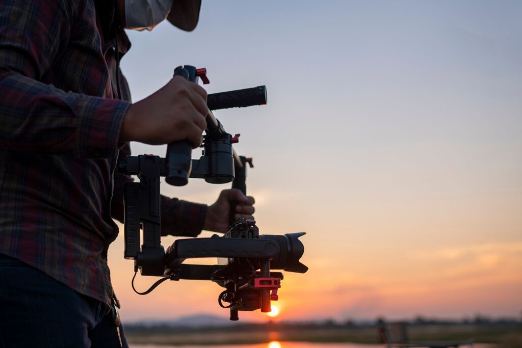 Closeup of a filmmaker using a gimbal stabilizer and a camera at sunset