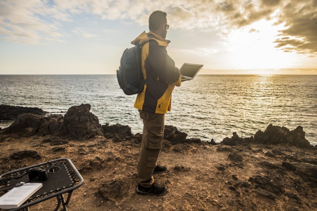 Digital nomad traveler man at work look an amazing golden sunset on the ocean