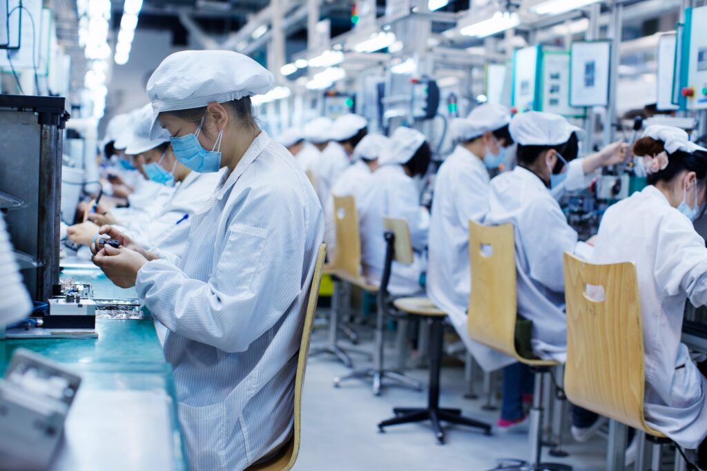 Group of workers at small parts manufacturing factory in China, wearing protective clothing, hats