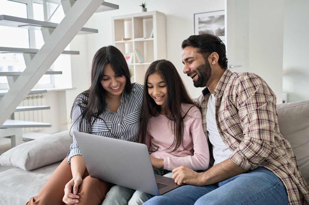 Happy indian family with teenage daughter having fun using laptop at home.