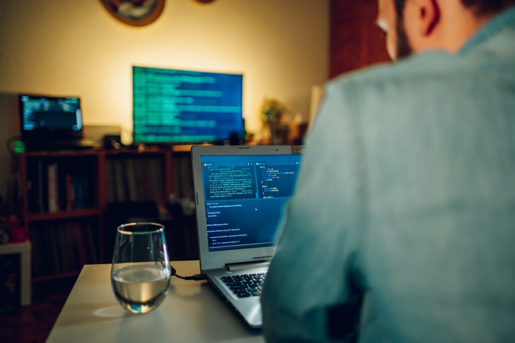 Rear view of a software engineer sitting at the home office and looking at code on a computer.