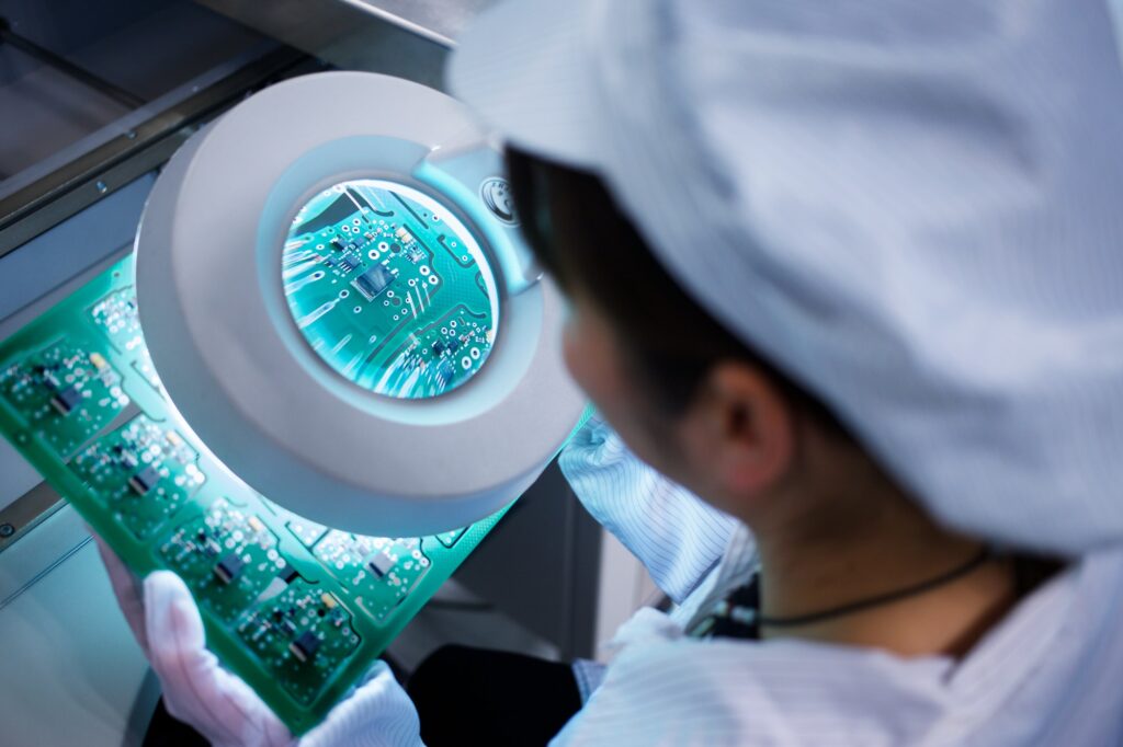 Worker at small parts manufacturing factory in China looking through magnifier at microchips