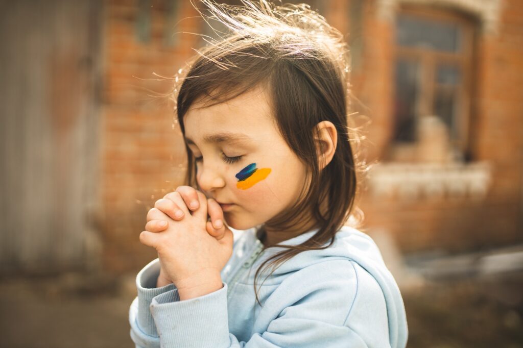 A girl with Ukrainian symbols on her face prays. A child from Ukraine. Ukrainian. Pray for Ukraine.