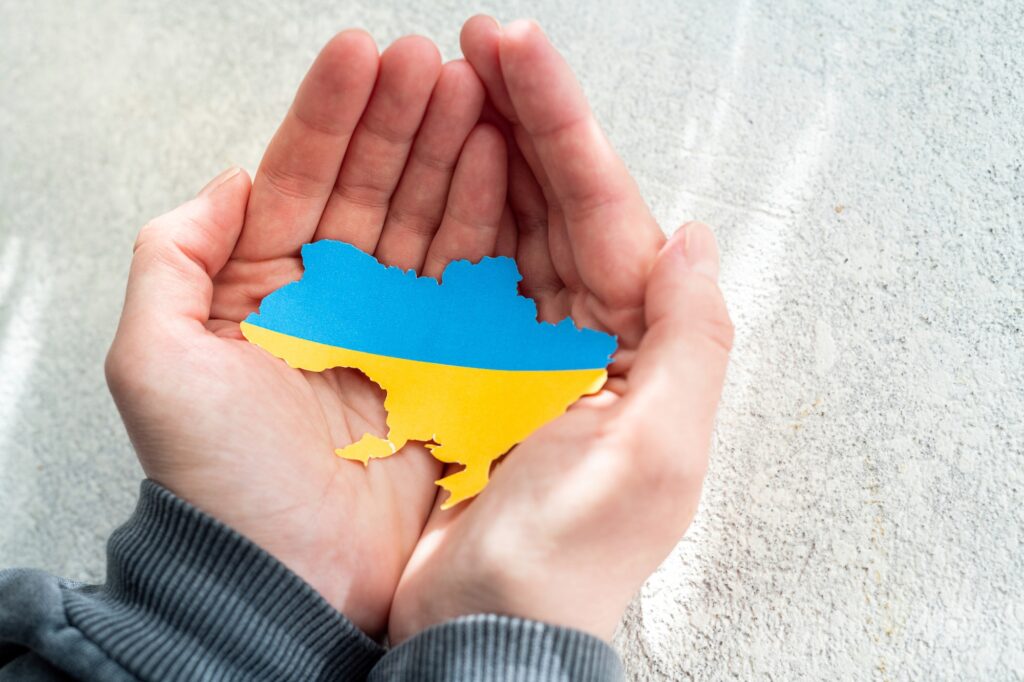 Hands holding the national flag of Ukraine in the shape of the borders of Ukraine