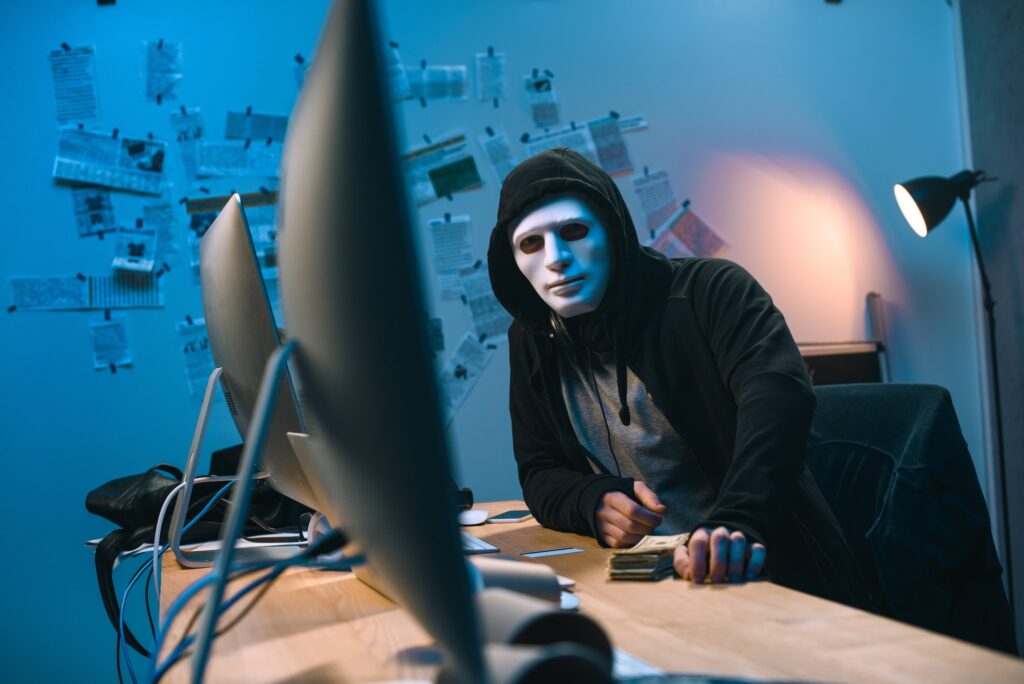 hooded hacker in mask with stack of money on desk