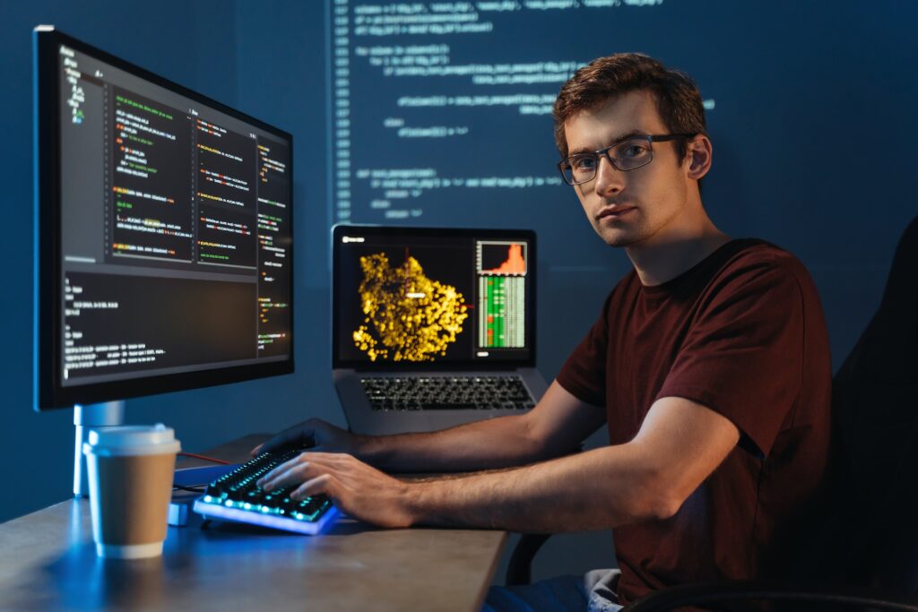 Intelligent male programmer working on pc writing brand new code at home office, looking at camera