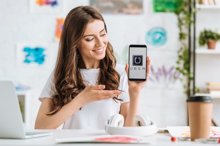 KYIV, UKRAINE - APRIL 17, 2019: Pretty young woman girl pointing with hand at smartphone with Uber