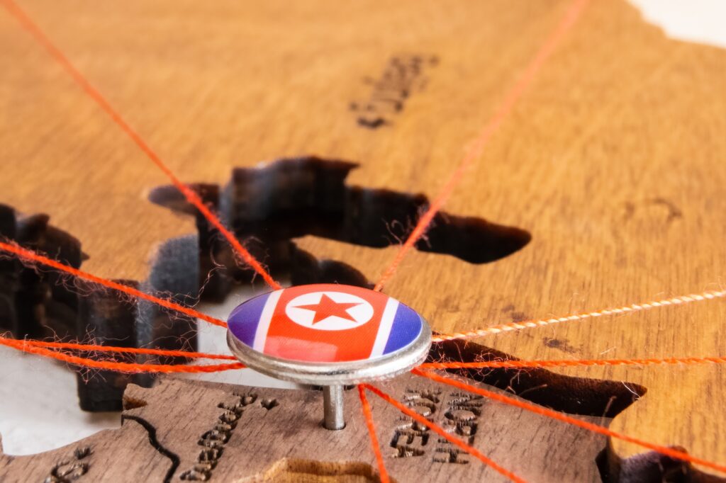 North Korea flag on the pushpin and red thread on the wooden map, close up