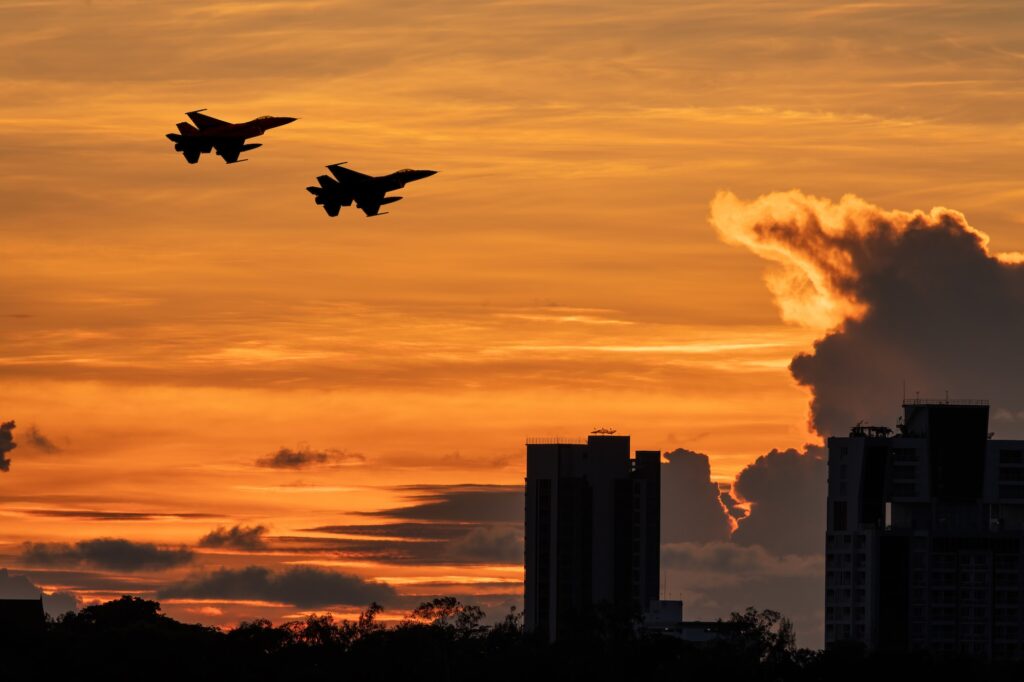 Silhouette team military aircraft flying over city building landscape with beautiful sun sky backgro