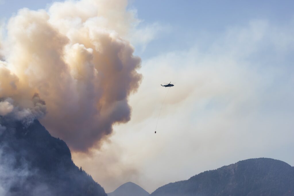 Wildfire Service Helicopter flying over BC Forest Fire and Smoke on the mountain near Hope