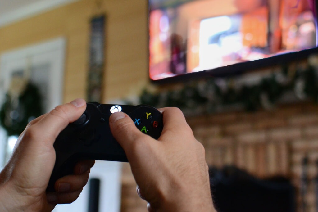 Holding a gaming controller while playing video games on a large TV mounted on the wall