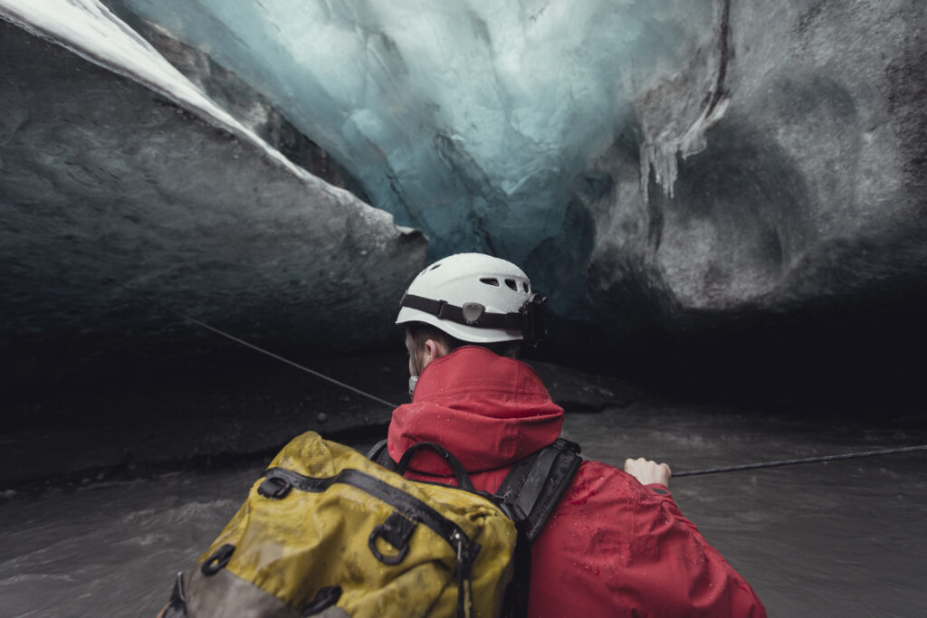 Man crossing river with rope in ice cave, Vatnajokull Glacier, Vatnajokull National Park, Iceland