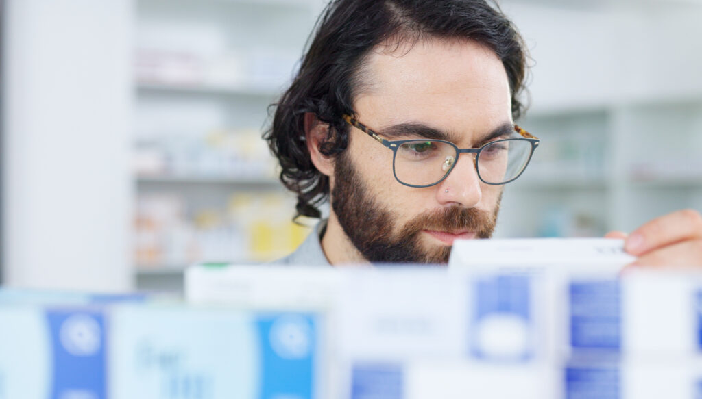 Man with glasses choosing medication on a shelf in a pharmacy. Customer with glasses browsing in ai