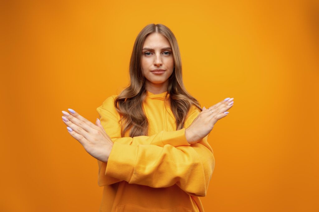 Portrait of attractive girl showing reject sign with crossed arms in studio