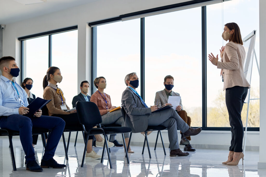 Female CEO giving presentation to group of business people during coronavirus pandemic.