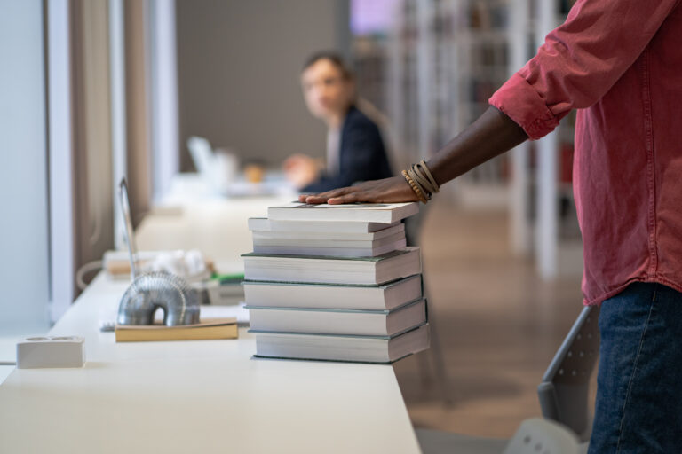 Hand hold stack of books on library table prepared to study material of higher education institution