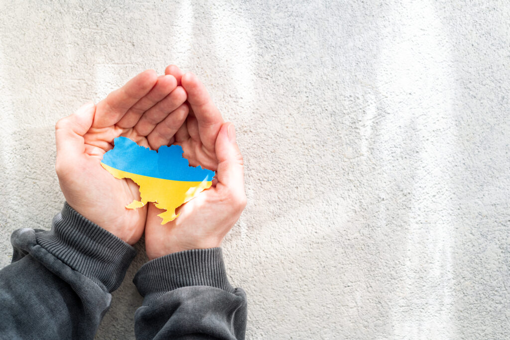 Hands holding national flag of Ukraine in the shape of the borders of Ukraine. Support for Ukraine