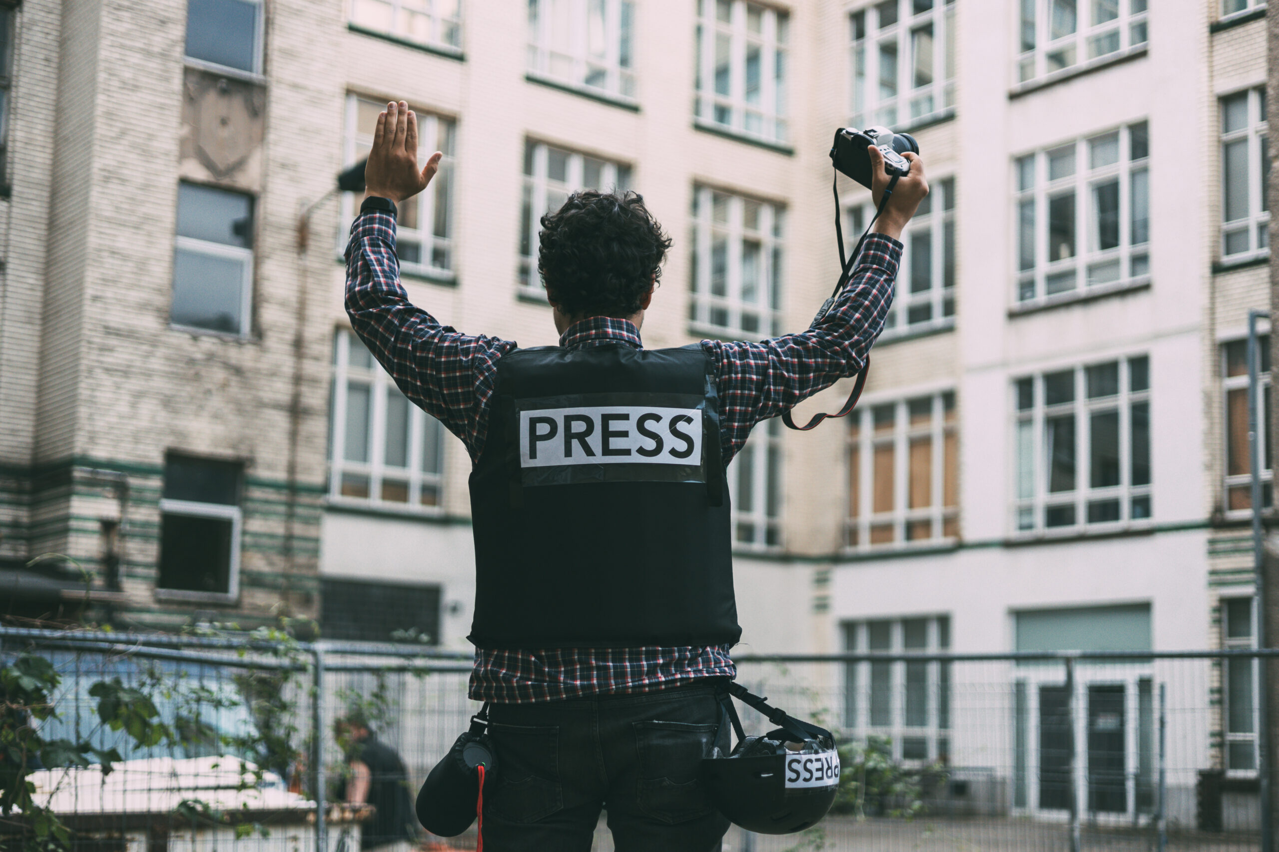 photojournalist in bulletproof vest holding his camera with his hands in the air