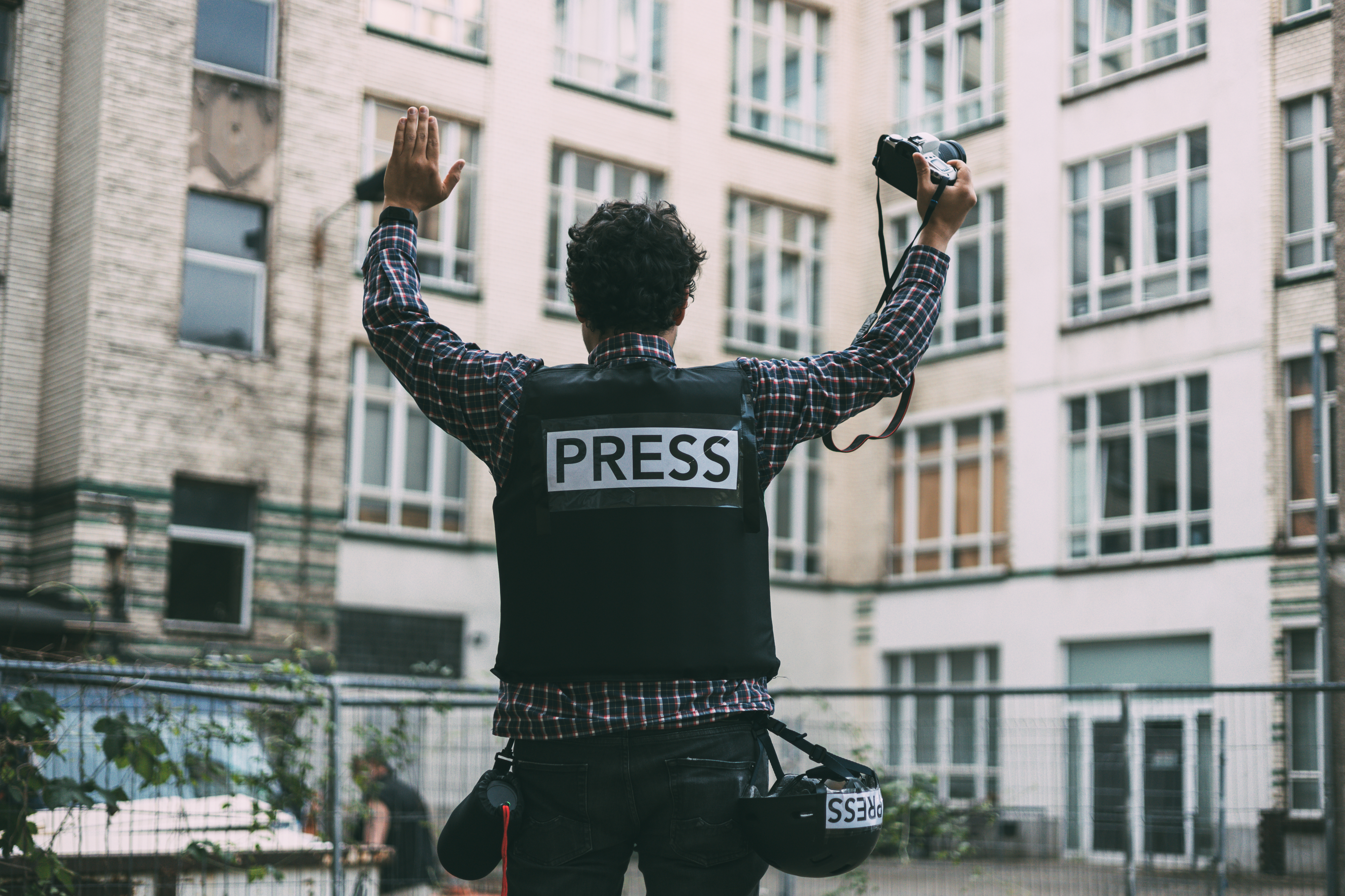 Photojournalist in bulletproof vest holding his camera with his hands in the air