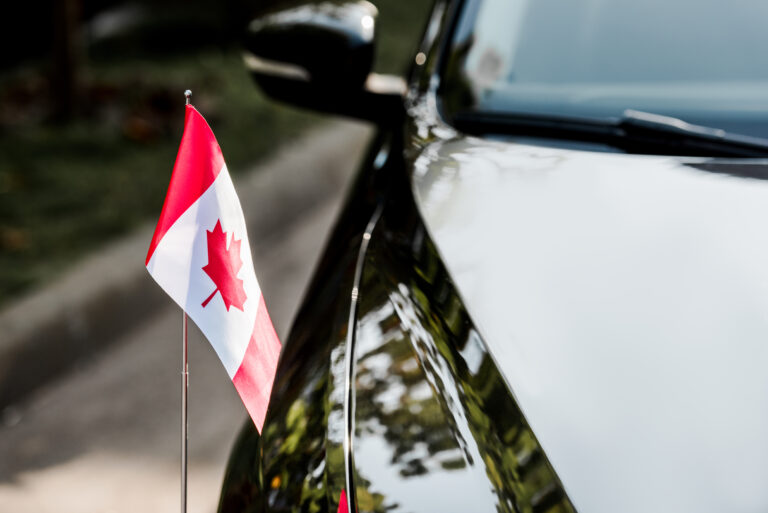 selective focus of canadian flag with maple leaf on black car