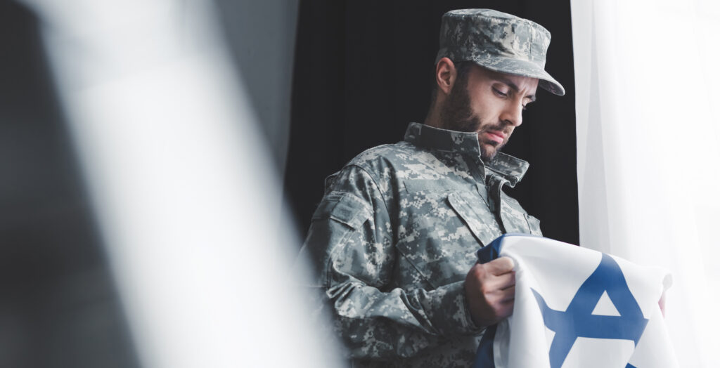 selective focus of pensive military man in uniform holding israel national flag while standing by