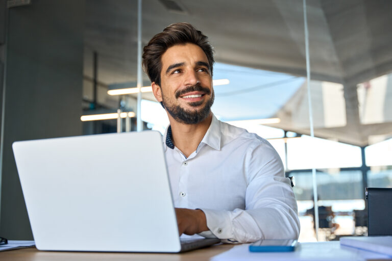 Smiling young Latin business man working at laptop computer in office.