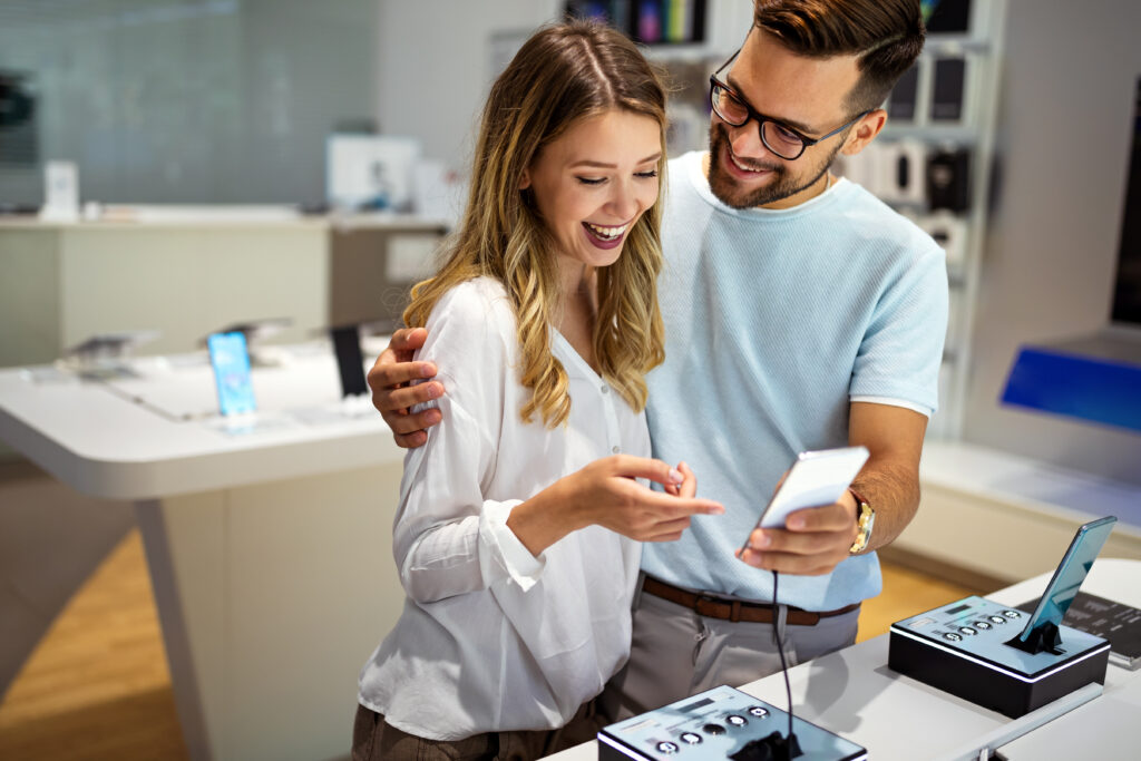 Young satisfied couple testing the new model of a smart cell phone from the desk in the tech store.