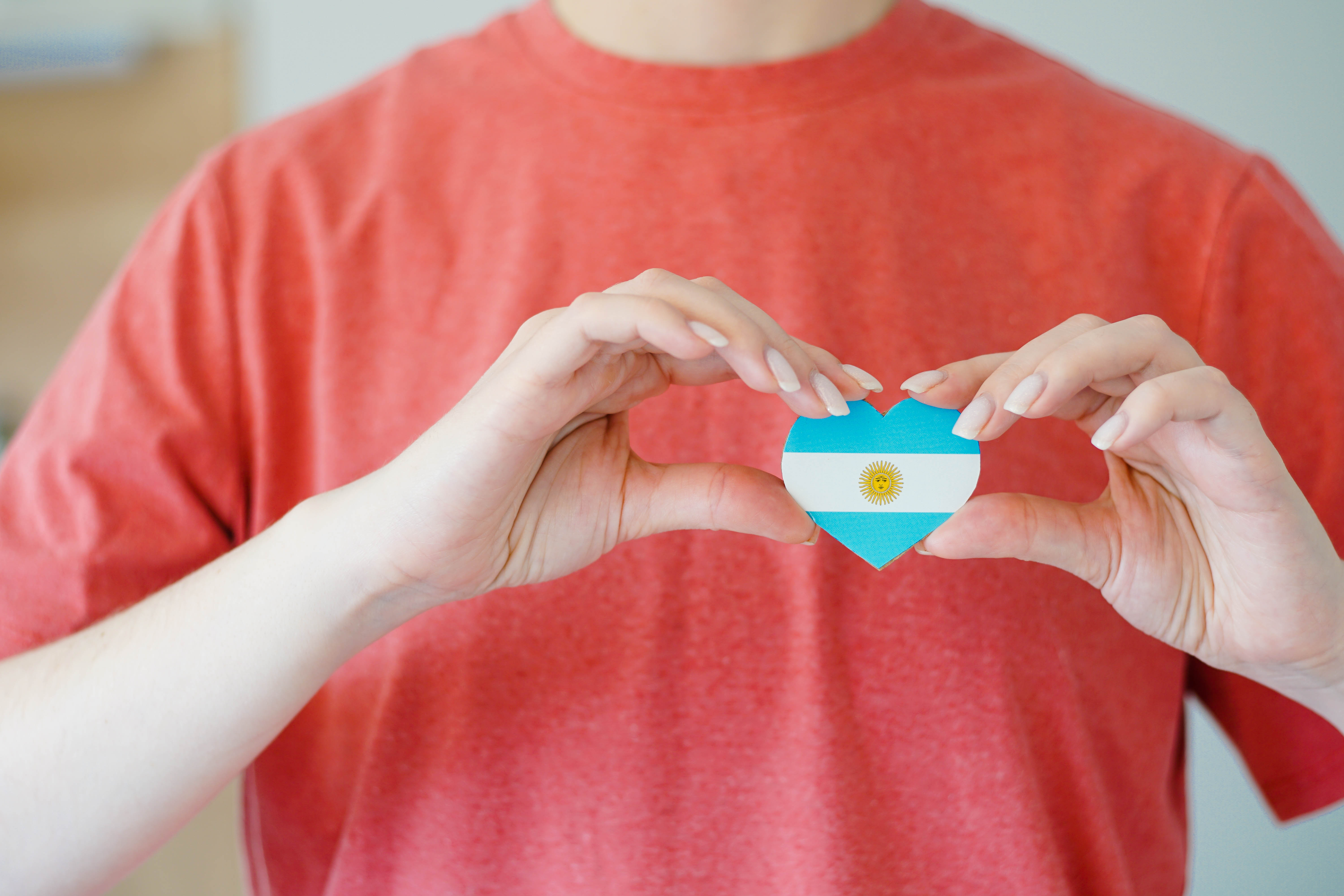 Young woman holding a heart in the form of a flag of Argentina.