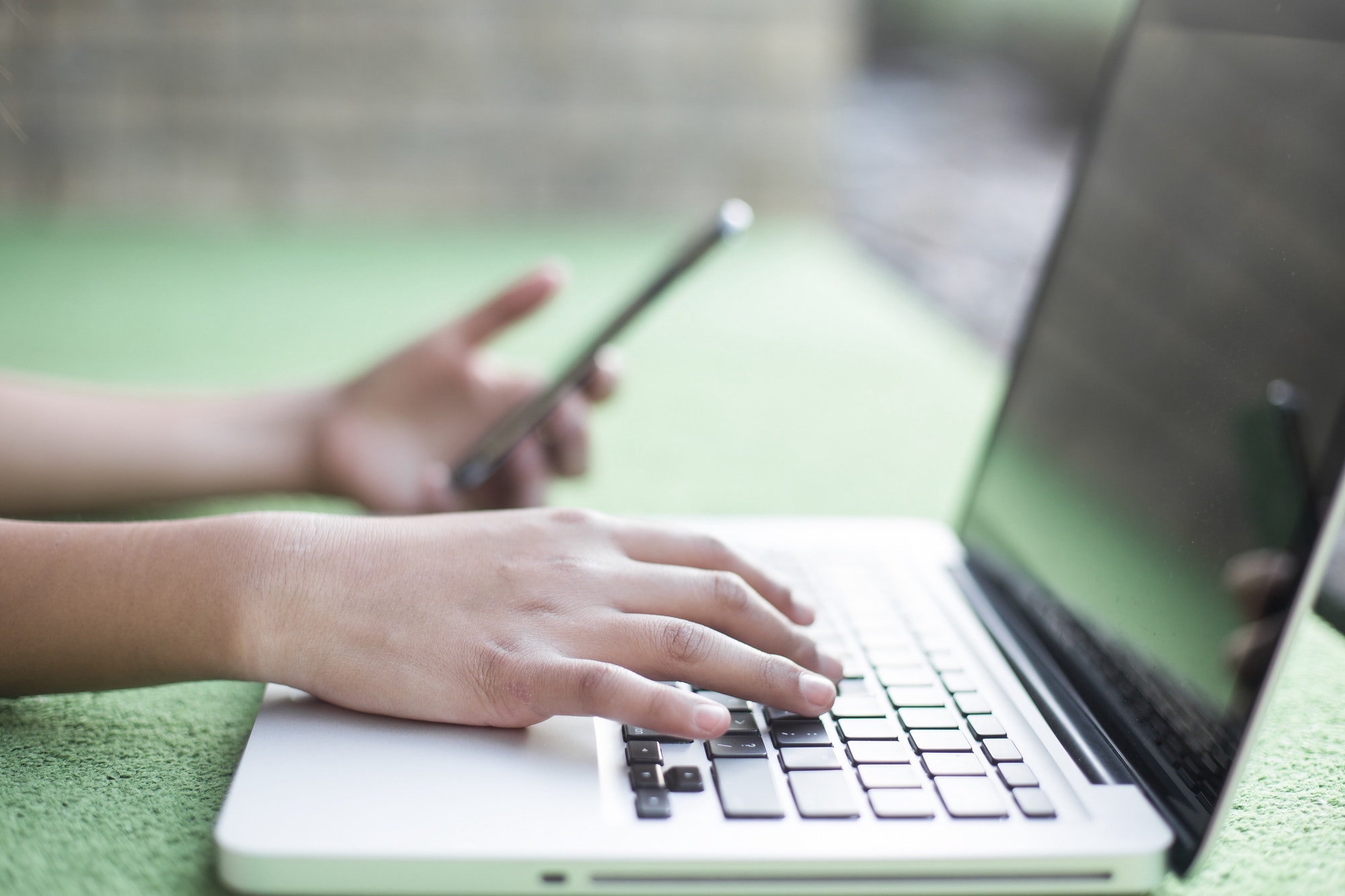 Girl typing on a laptop and using her iPhone