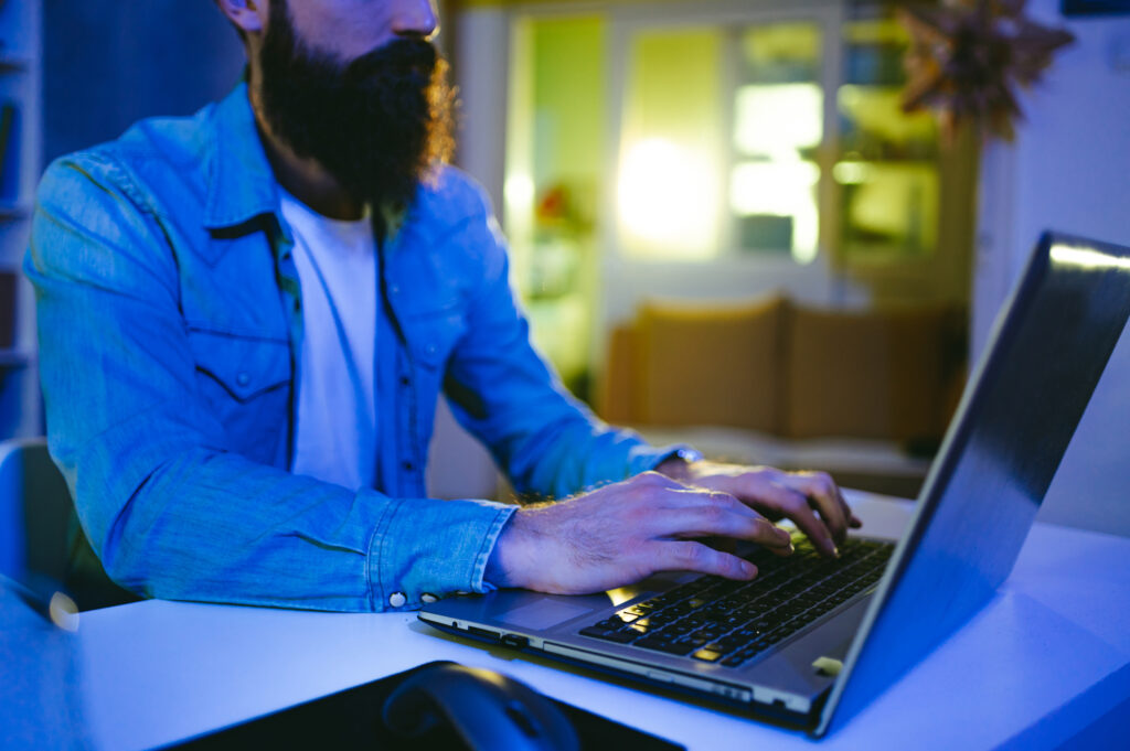 Hands of an AI developer typing on a laptop in his neon blue lighted home office.