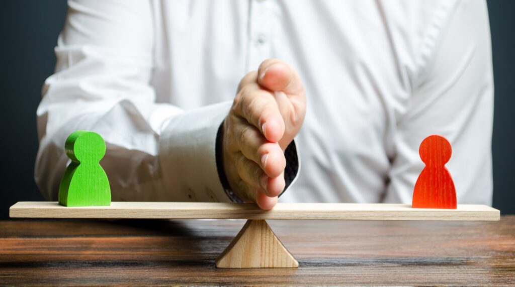 A man divides with his palm two figures of people of opponents on the scales