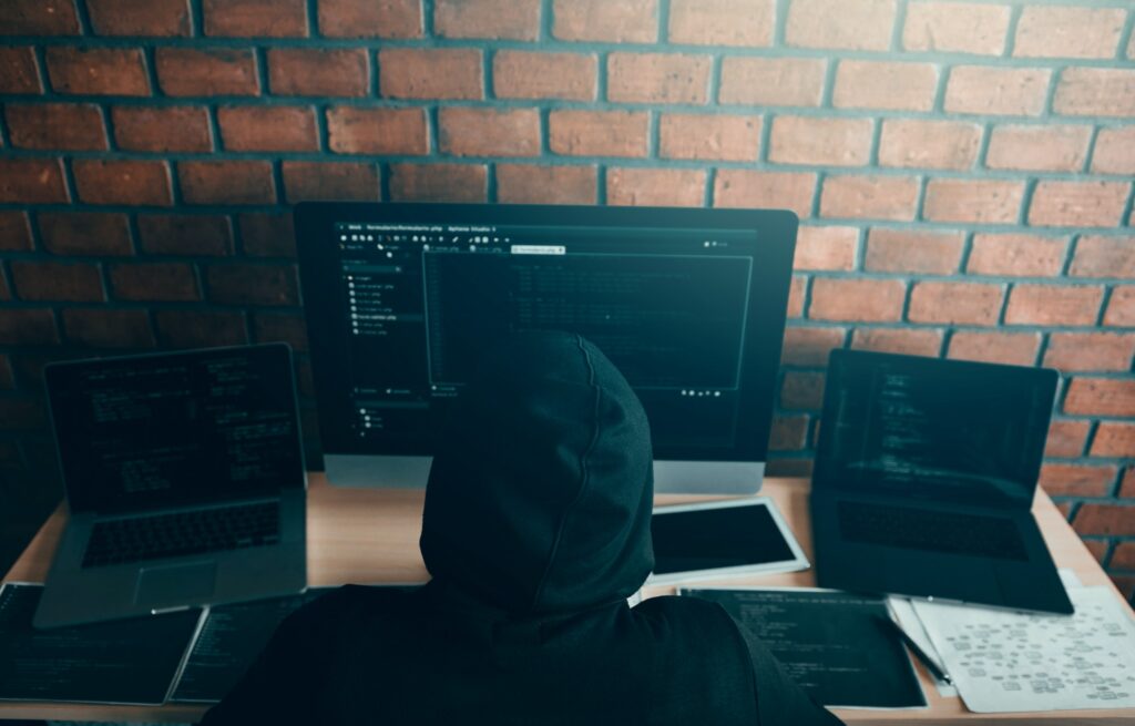 Hacker in the hood working with computer with hacking breaking into data servers.