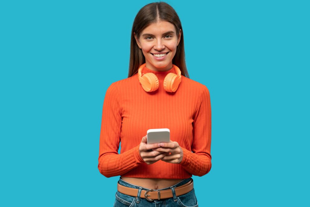 Woman with headphones on neck picking up cool track from her playlist on phone on blue background