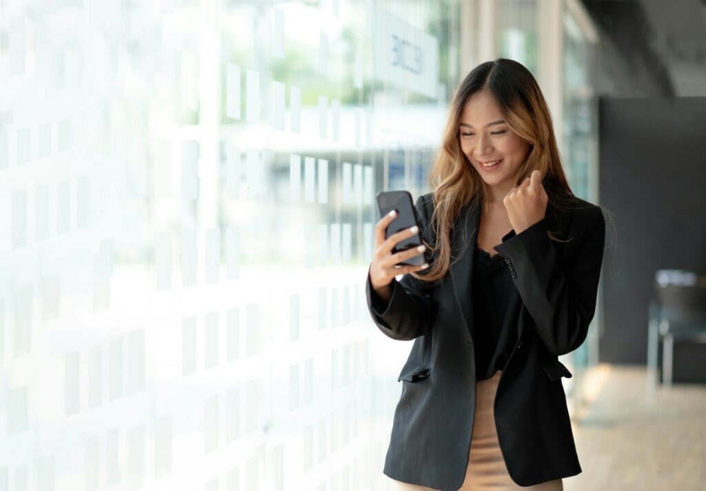 Beautiful asian woman using smartphone, exciting and celebrating with good news of business