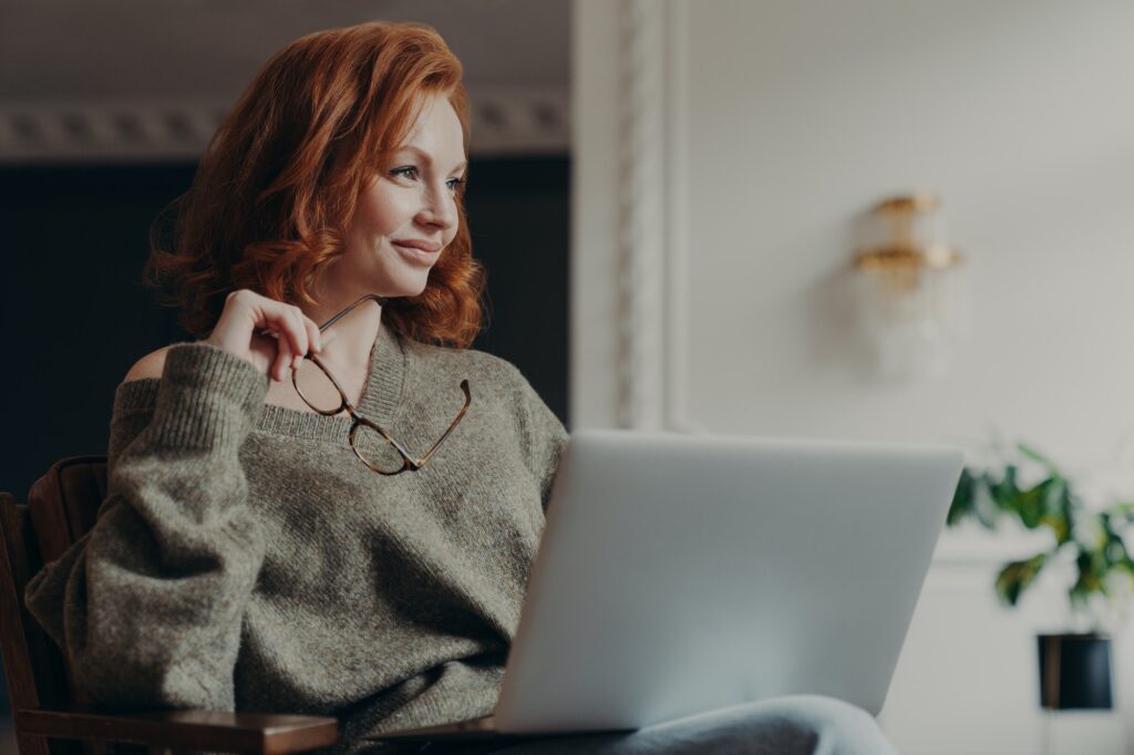 Experienced redhead female entrepreneur makes plans, looks aside with dreamy expression