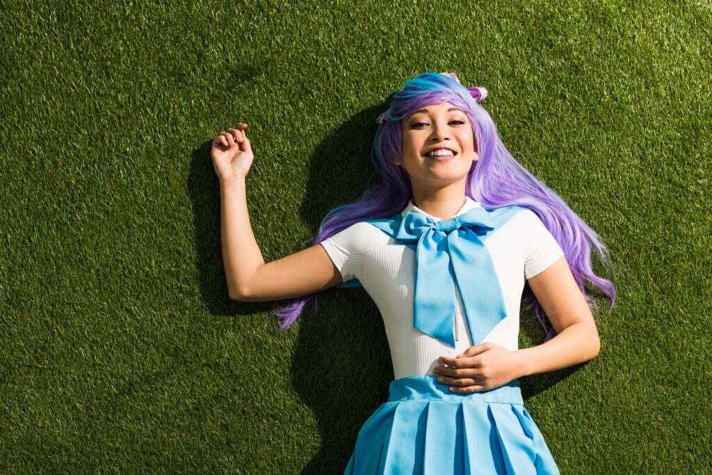 Smiling asian anime girl in purple wig lying on green grass