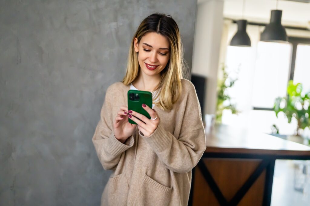 Smiling young woman chatting in social networks, working, using mobile applications at home.