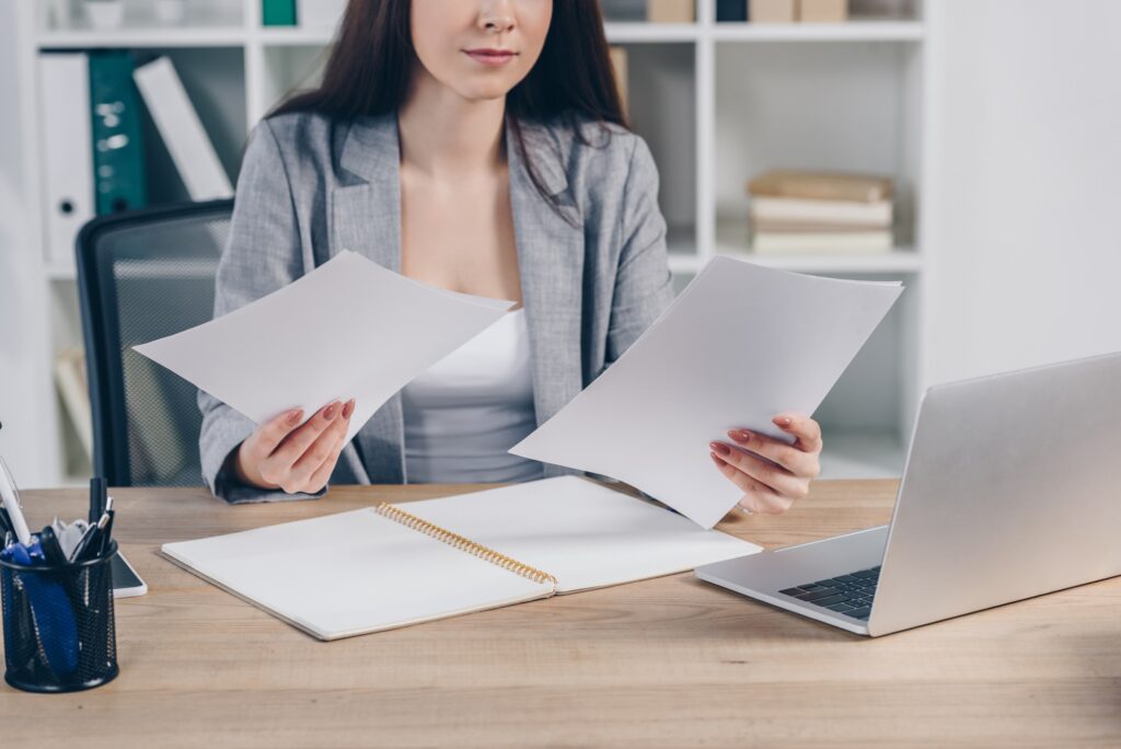 Cropped view of recruiter with papers and laptop at table in office