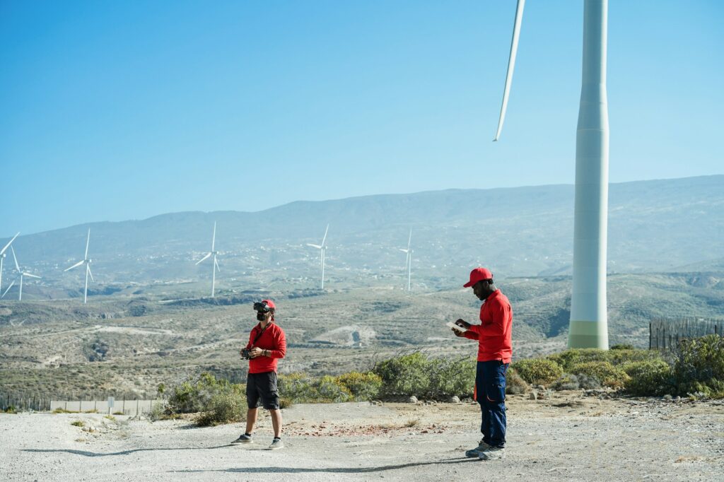 Engineers using virtual reality headset while working at windmill farm with tablet and drone