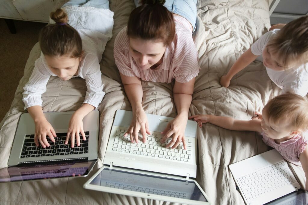 Mom and Three children lie on bed with laptops, concept digital addiction and working mom