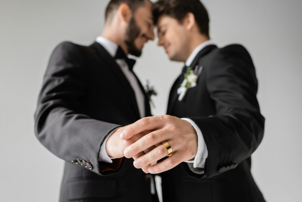 Side view of blurred same sex couple in formal wear with boutonnieres touching hands of each other