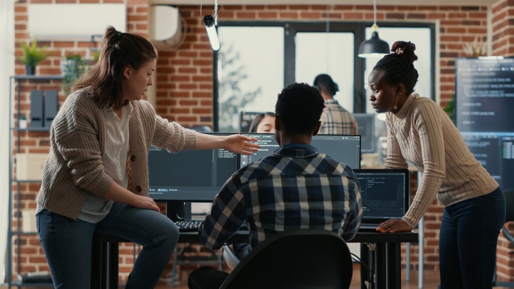 System engineer sitting on desk discussing with mixed team of coders about ai innovation