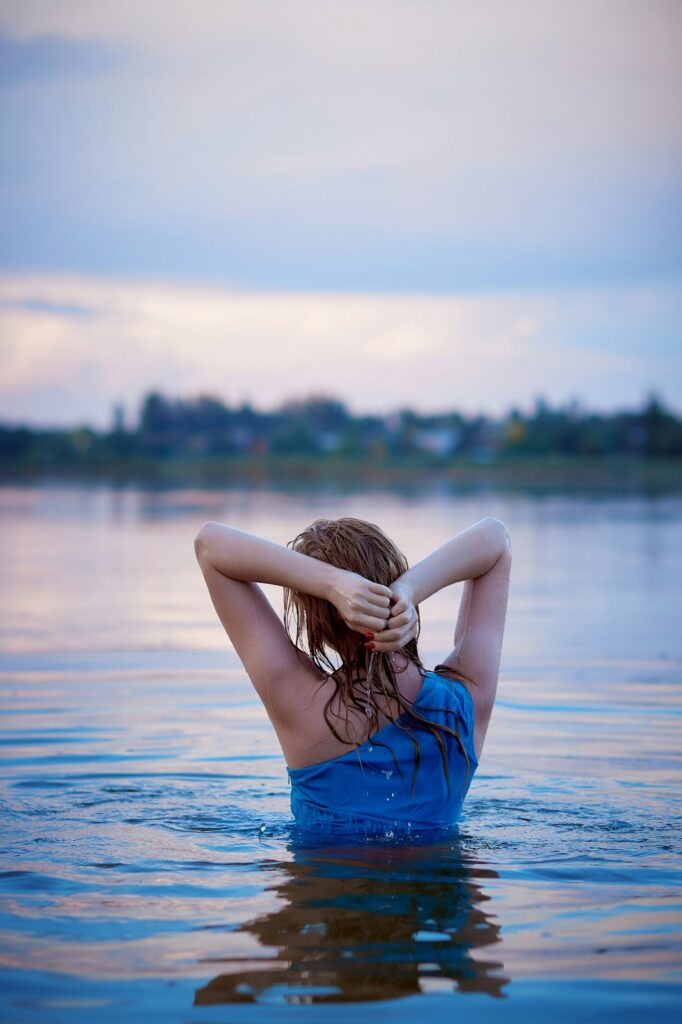 Aesthetic millennial sensual girl laying on blue cloth in water at golden sunset. Relaxing and enjoy