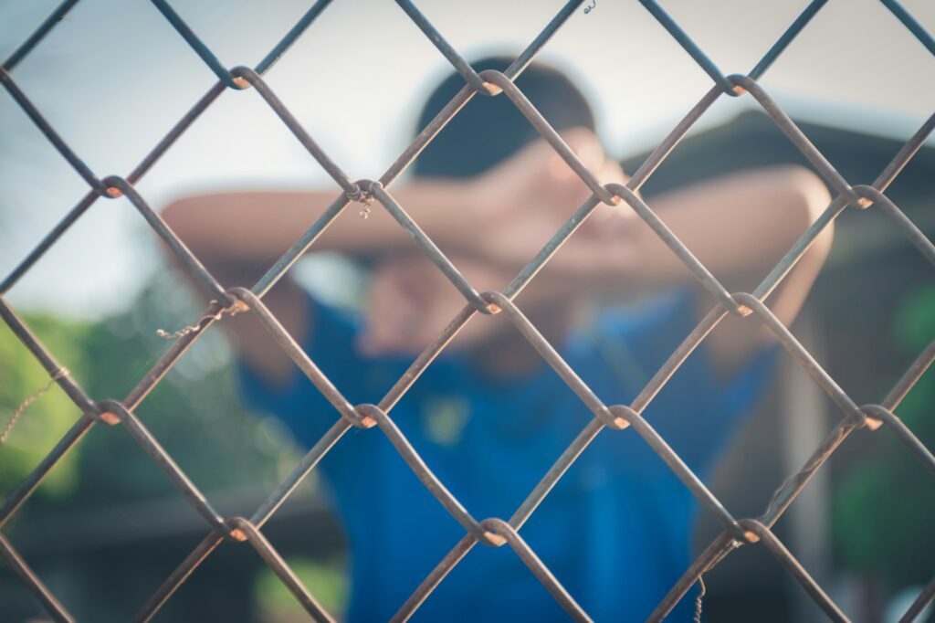 Asian kid boy crying behind a metal chain wire mesh fence