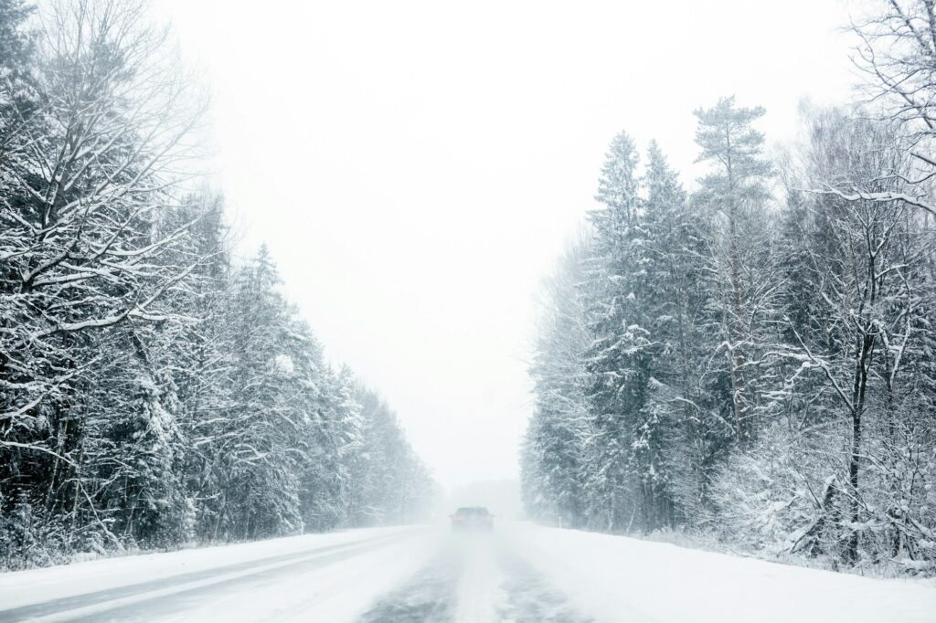 Car driving trough forest highway in snowstorm