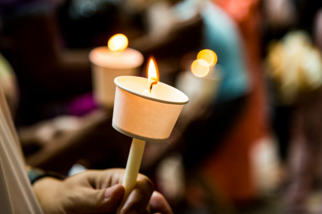 Closeup of people holding candle vigil in dark seeking hope