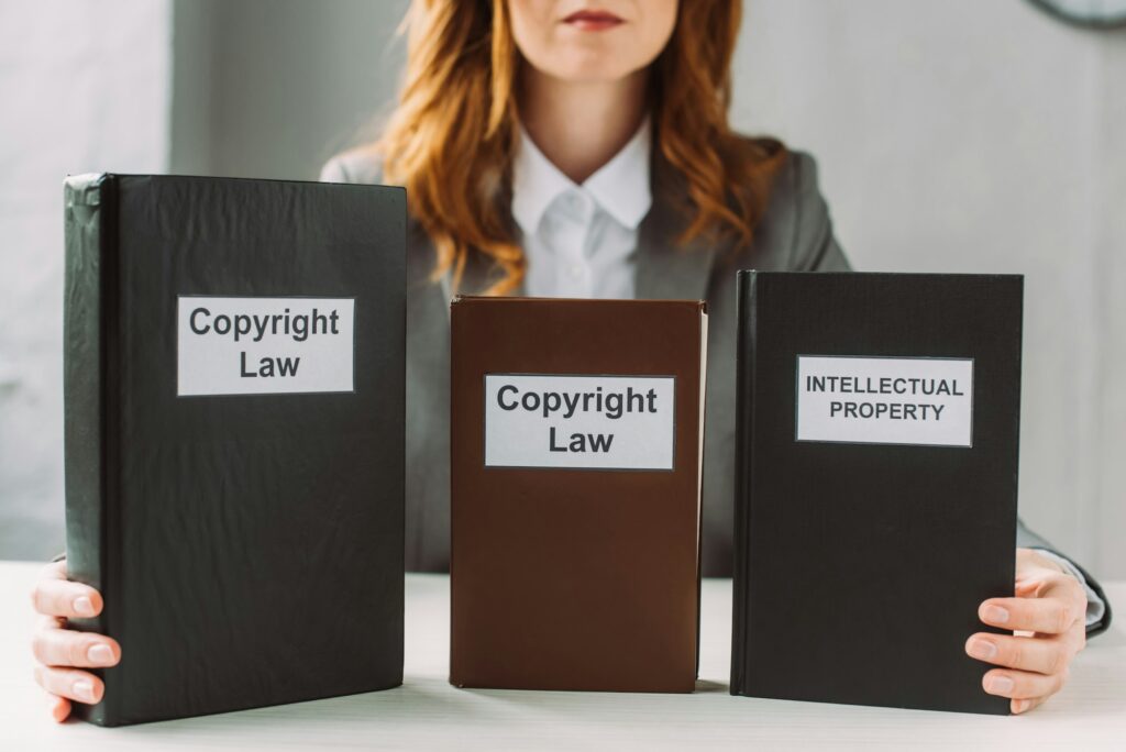 Cropped view of lawyer holding book with intellectual property and copyright law lettering on table