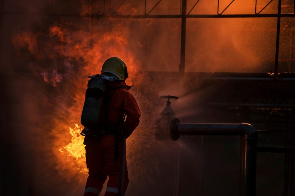 Firefighter in the training with fire hose nozzle spraying high pressure water to fire