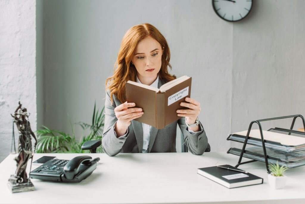 Focused female lawyer reading book with copyright law lettering, while sitting at workplace