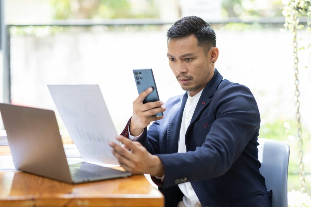 Take picture, Asian Businessman sitting at workplace desk and Taking Photograph Of Document In Offic